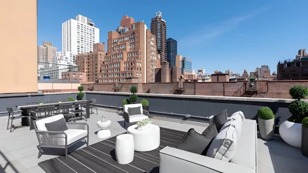 White couches with gray pillows on a rooftop terrace with a view of towering buildings
