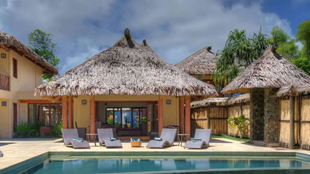 A house with a thatched roof with sun loungers and a pool in front of it