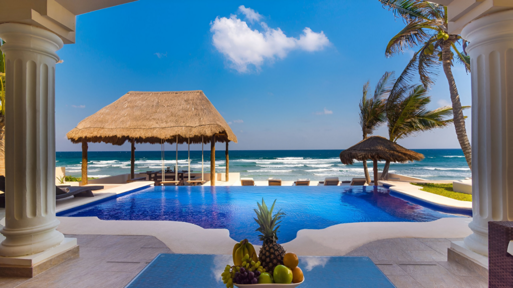 A serene pool and patio with a thatched roof, offering a breathtaking view of Tulum beach