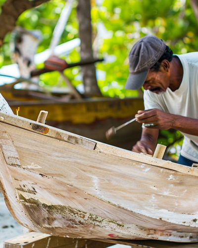 Artisan crafting a traditional boat in Turks and Caicos with a tropical forest in the background.