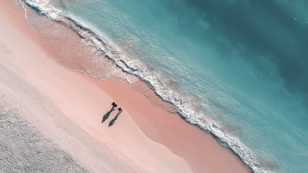A minimalist aerial view of Dunmore Town’s Pink Sand Beach with soft blush sand and crystal-clear turquoise waters in a serene coastal setting.